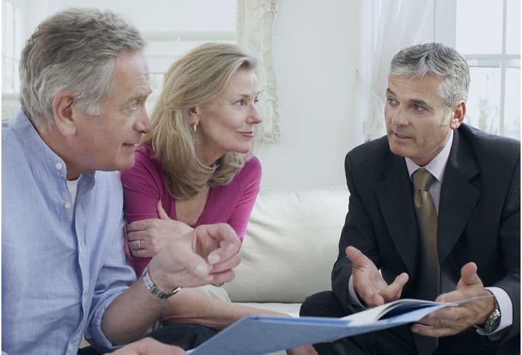 Beratungsgespräch mit älterem Paar und Geschäftsmann Ein älteres Paar sitzt auf einem Sofa und spricht mit einem Geschäftsmann im Anzug, der ihnen Unterlagen zeigt