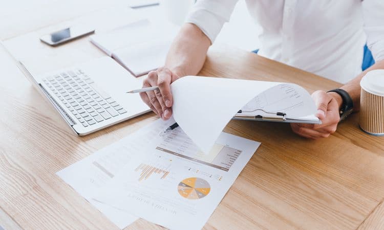 Lohnkosten im Blick: Auswertungen und Reports in der Lohnbuchhaltung Person analysiert Geschäftsdiagramme mit Klemmbrett, Laptop und Stift am Schreibtisch